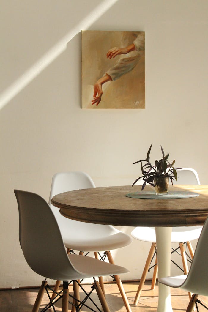 brand-03 Sunlit minimalist dining room with round table, chairs, and painting.