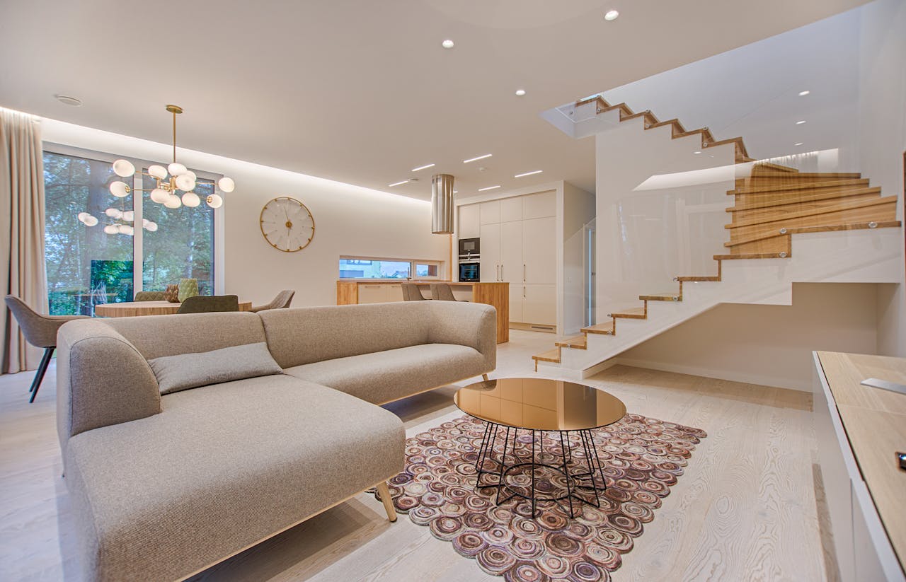 Services-01 Contemporary living room with neutral tones, a sleek sofa, and elegant wooden staircase.