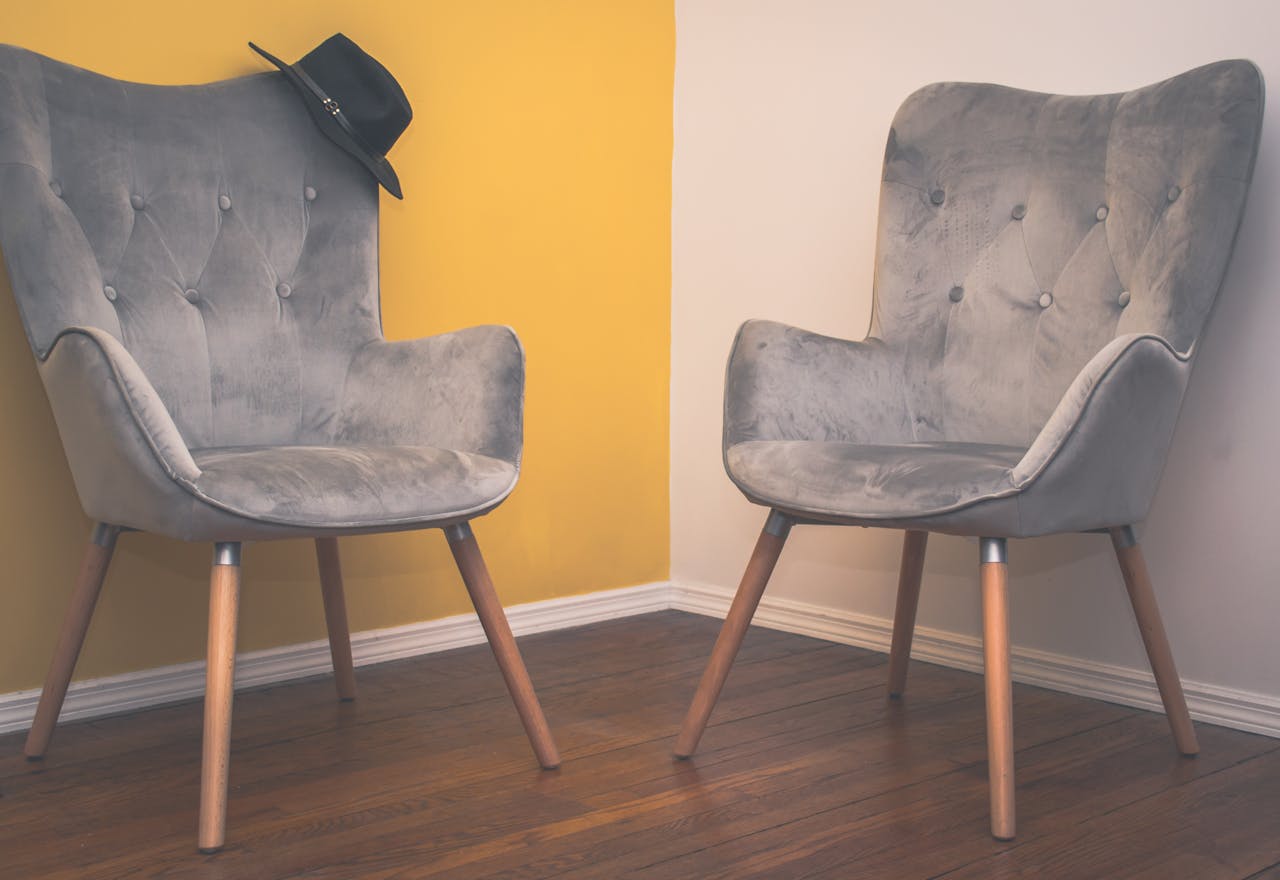 creative Two contemporary gray armchairs in a minimalist interior with a yellow accent wall and wooden flooring.